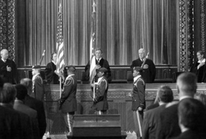 Black and white image of male and female judges wearing black judicial robes standing as a military color guard carries the American and Ohio flags into the courtroom of the Thomas J. Moyer Ohio Judicial Center.