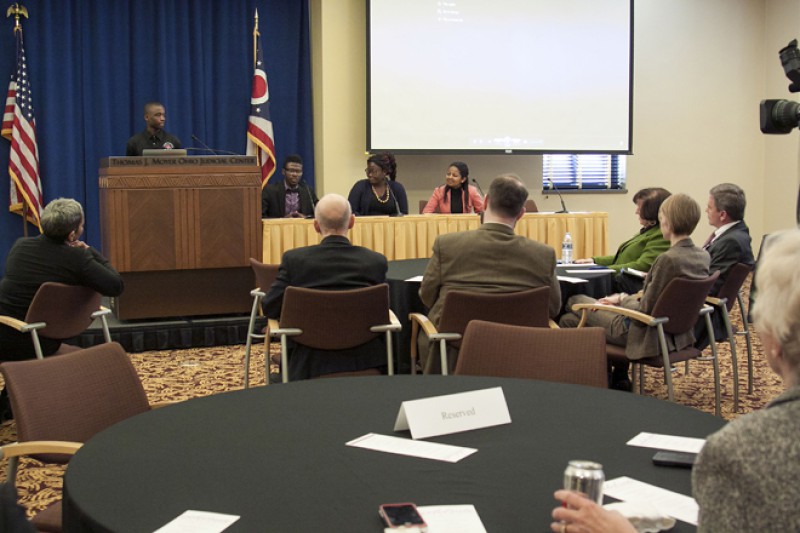 Image of a young African American man speaking from behind a podium to a group of people.