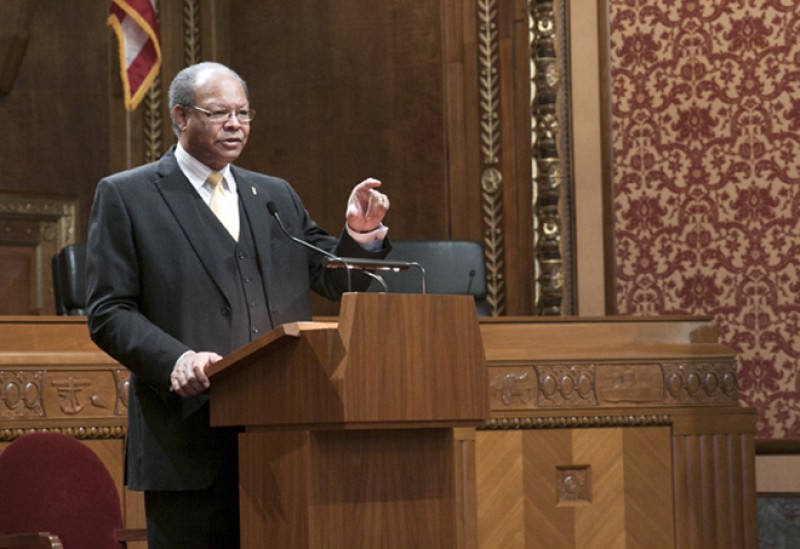 Image of an African American man wearing a dark three-piece suit speaking from behind a podium in the courtroom of the Thomas J. Moyer Ohio Judicial Center